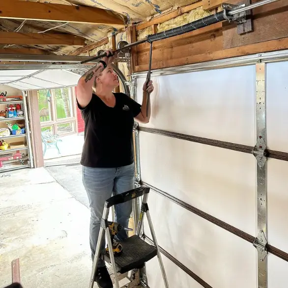 Woman repairing garage door spring on ladder.